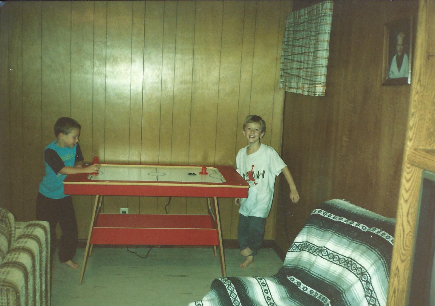 Two boys playing air hockey in a wood-paneled basement