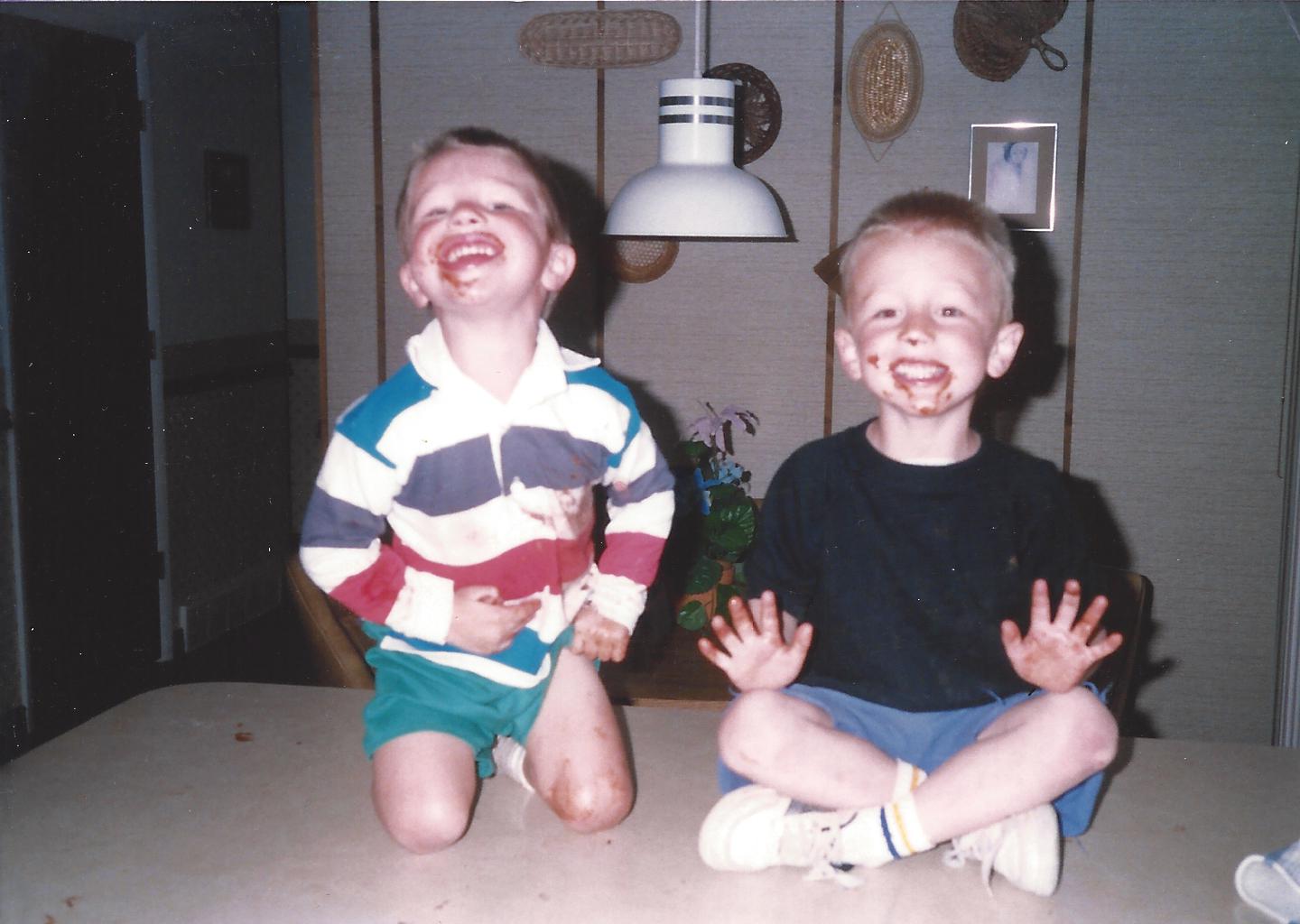 Two boys with chocolate-smeared faces on top of the kitchen table